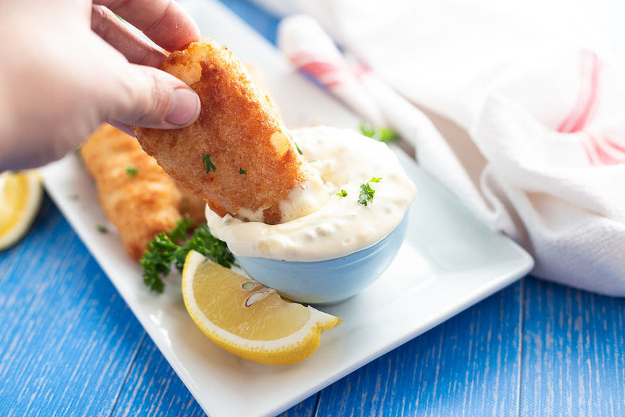 Fried fish being dipped into homemade tartar sauce in a light blue bowl