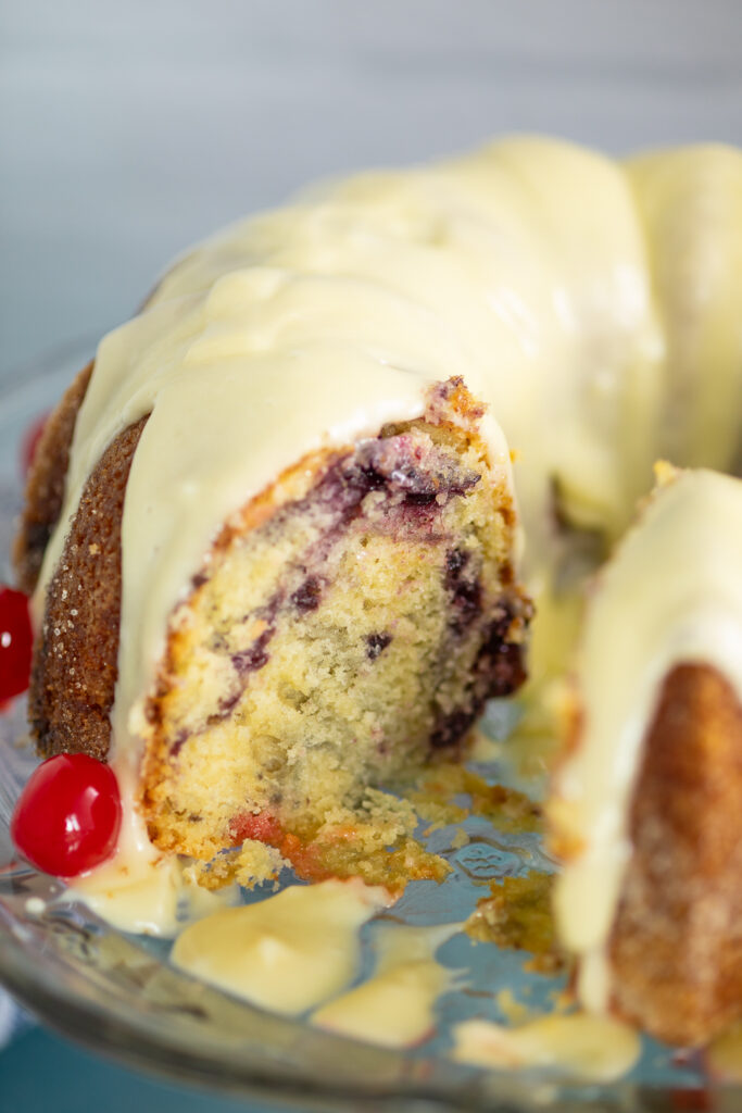 An overhead view of the full cherry marble cake topped with cream cheese glaze on a glass plate, with a slice missing showing the cherry swirl inside.