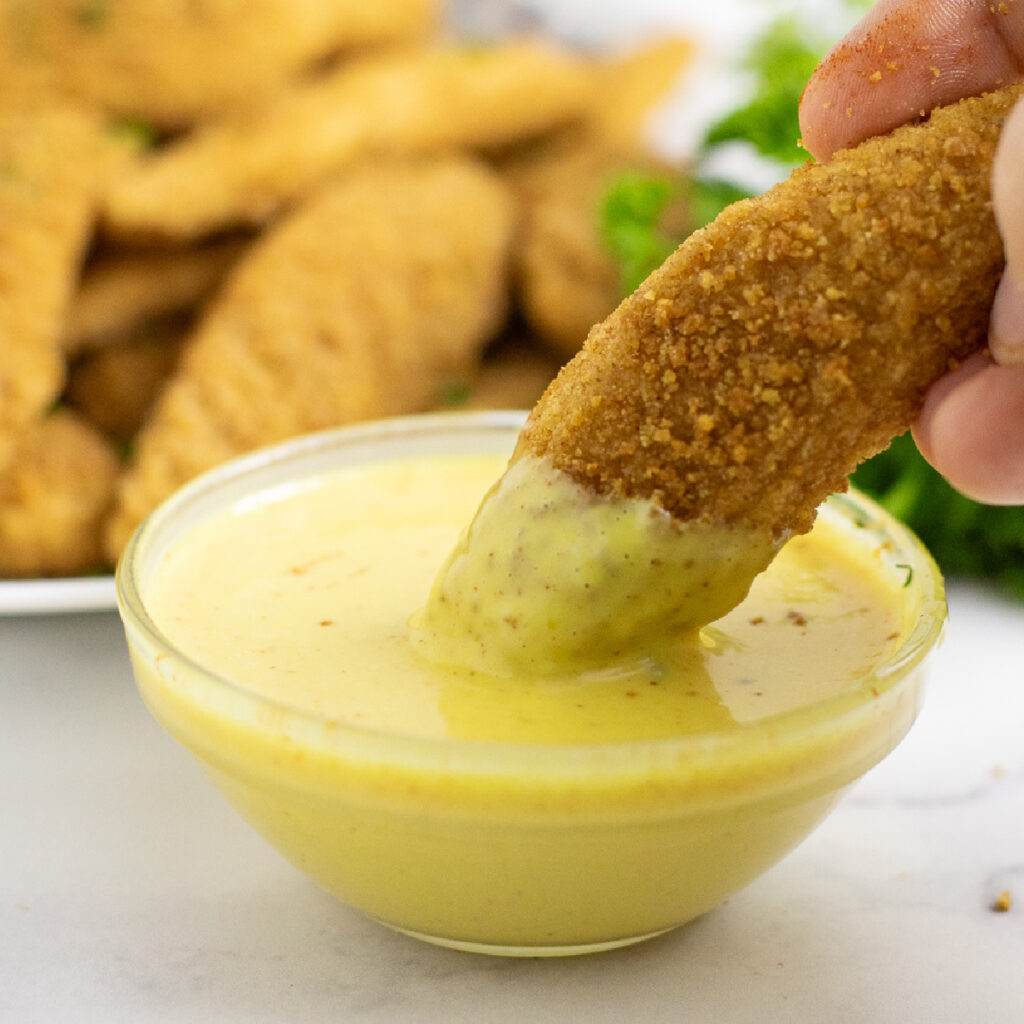 Chicken tender being dipped into a small bowl of homemade honey mustard dip