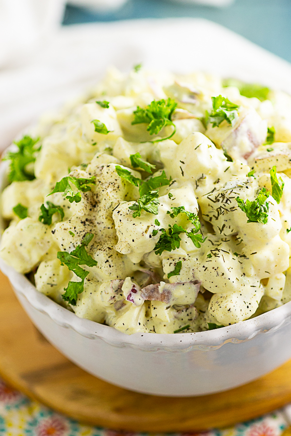 Close up overhead view of southern potato salad topped with parsley and dill sitting on a wooden trivet