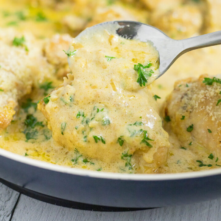 Creamy dijon chicken in a skillet with a spoon spooning more sauce on top.
