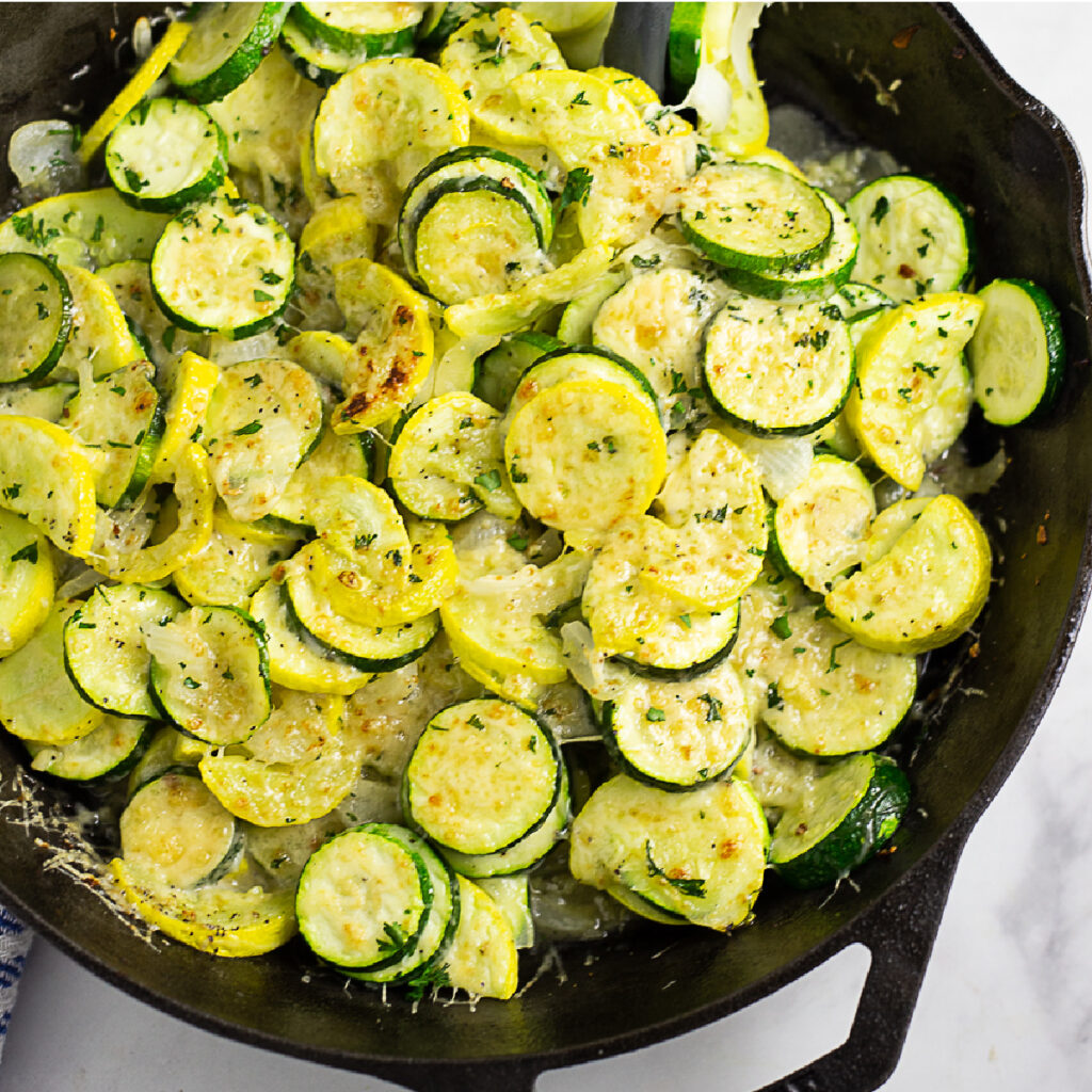 Overhead view of a large cast iron skillet with sauteed zucchini and squash topped with grated parmesan cheese