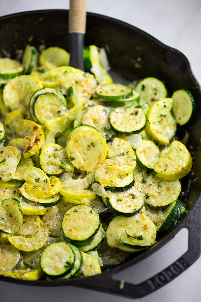 Sauteed Zucchini and squash in a cast iron skillet topped with grated parmesan with a wooden spoon in the middle