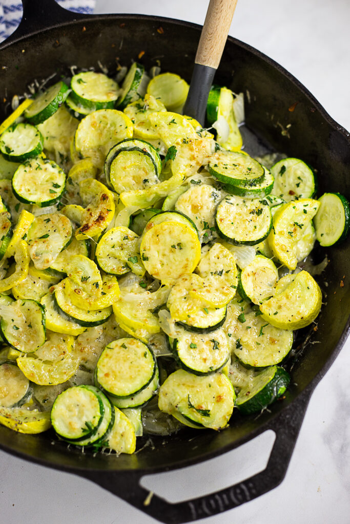 Overhead view of a large cast iron skillet with sauteed zucchini and squash topped with grated parmesan cheese
