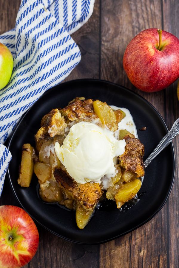 Overhead picture of apple cobbler topped with vanilla ice cream on a plate surrounded by a linen napkin and fresh apples