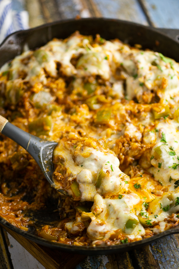 Unstuffed peppers covered in melted mozzarella in a cast iron skillet with a spoon in the middlw