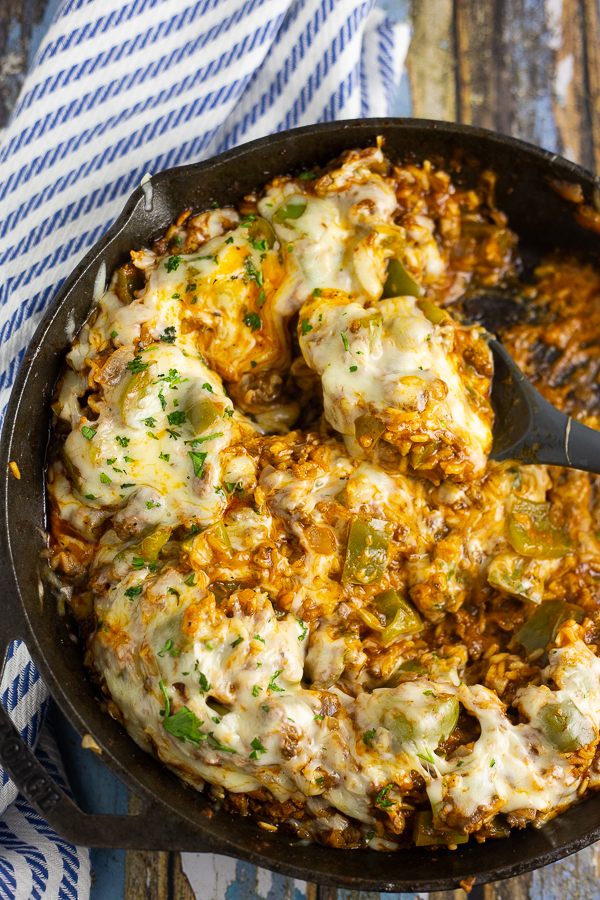 Unstuffed peppers covered in melted mozzarella in a cast iron skillet with a spoon in the middle