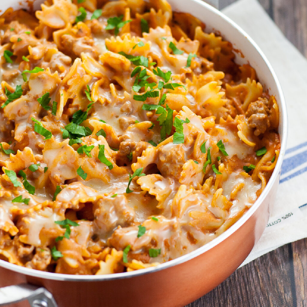 Creamy sausage pasta in a copper pot topped with melted cheese and fresh chopped parsley