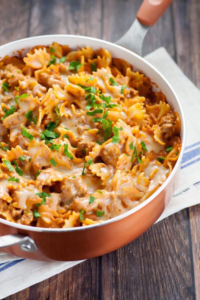 Creamy sausage pasta in a copper pot topped with melted cheese and fresh chopped parsley