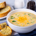 Crockpot broccoli cheese soup in a bowl next to crusty buttered bread