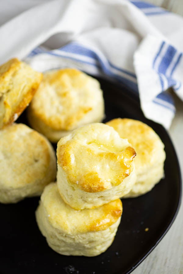 Overhead view of a stack of biscuits on a black matte plate with a white potato sack linen