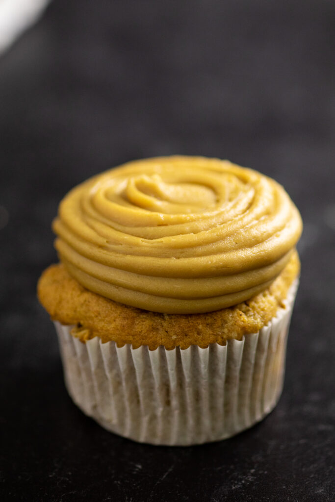 Caramel frosting typed onto a sweet potato cupcake in a wrapper on a black marble backdrop