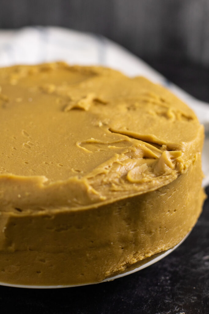 A round layer cake covered in caramel frosting on a black marble background with a white linen napkin behind