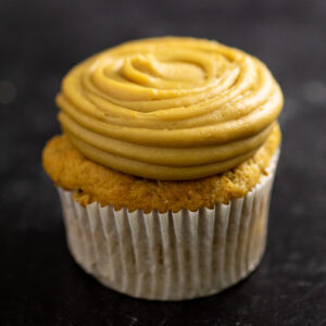 Piped caramel frosting on a sweet potato cupcake in a wrapper on a black marble background
