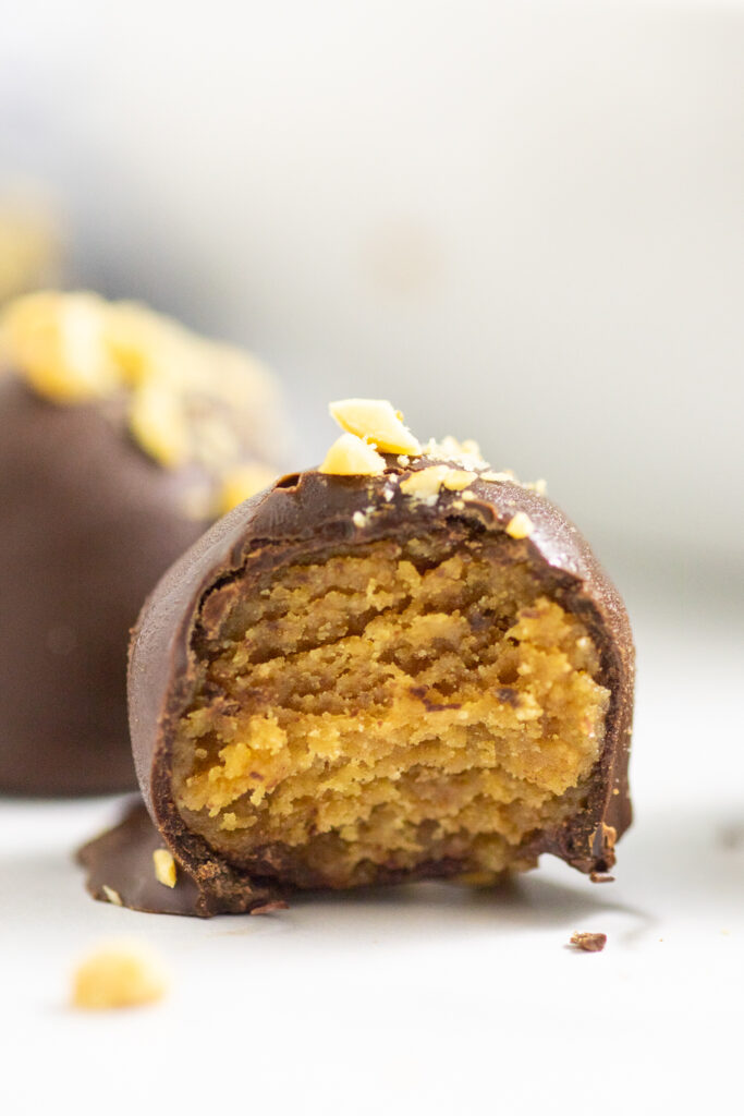 Close up of a Nutter Butter Ball with a bite taken out showing the peanut butter cookie truffle center on a white background with another ball behind it.