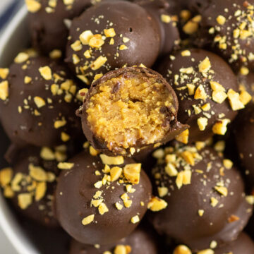 A pile of Nutter Butter Balls coated in chocolate and topped with chopped peanuts, and the top ball has a bite taken out showing the peanut butter ball center.