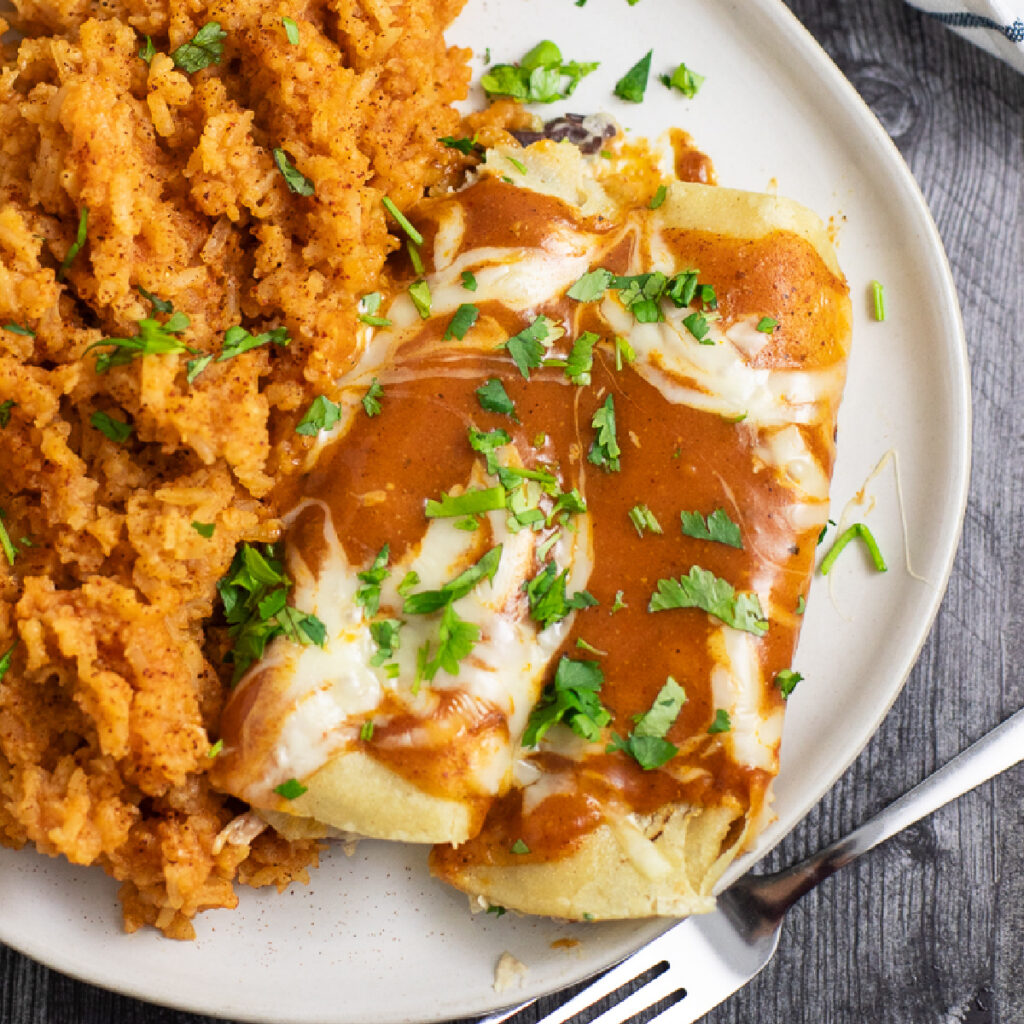 Overhead view of two bean enchiladas on a plate next to Spanish rice, topped with fresh cilantro.