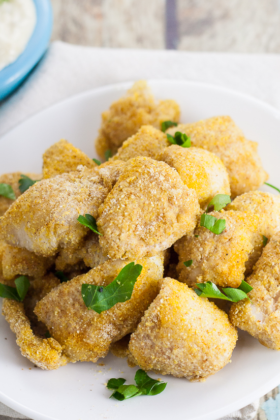 Cornmeal coated baked catfish nuggets topped with chopped fresh green parsley on a white plate on a rustic blue wood background