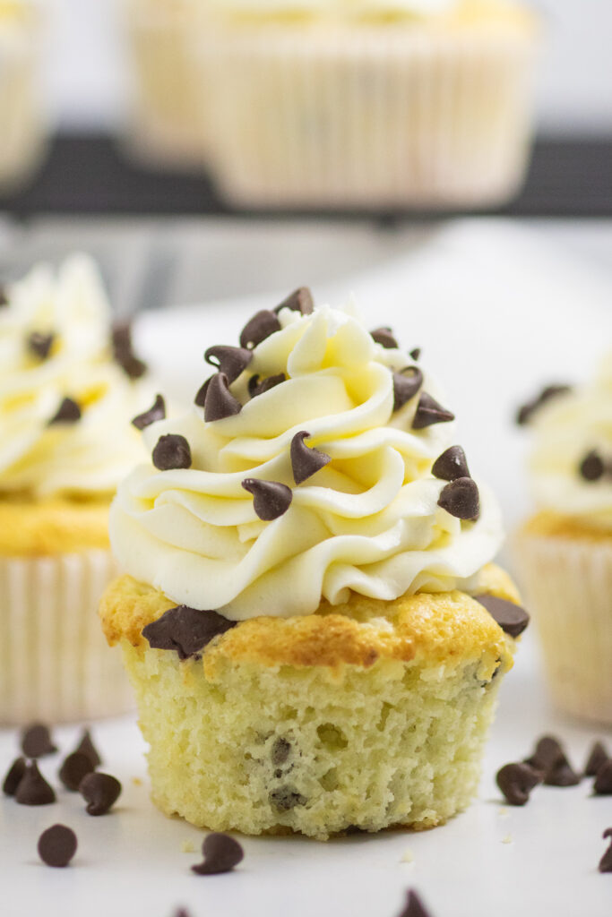 Chocolate Chip Cupcake topped with piped buttercream and mini chocolate chips in front of 2 more cupcakes with mini chocolate chips all around.