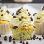 Chocolate Chip Cupcake topped with piped buttercream and mini chocolate chips in front of 2 more cupcakes with mini chocolate chips all around.