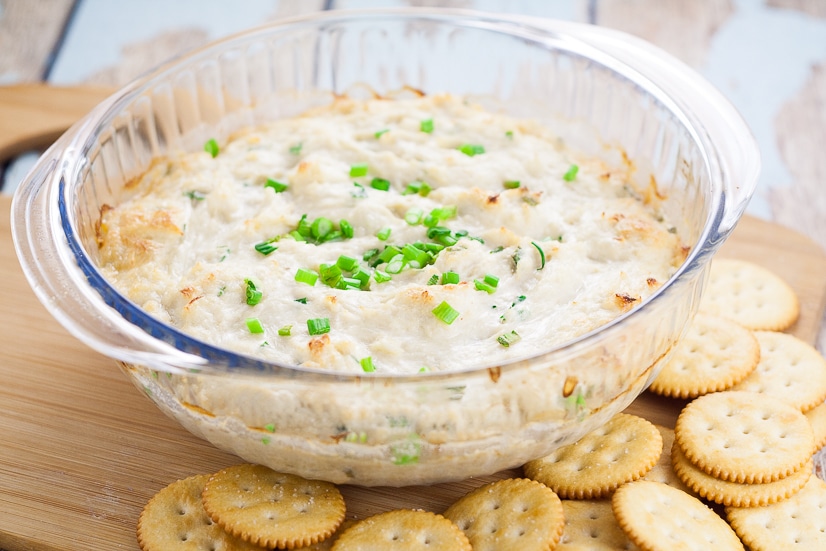 Crab rangoon dip in a glass bowl topped with green onions, surrounded by butter crackers