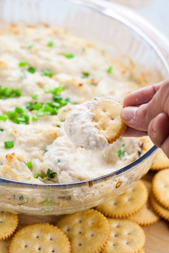 Butter cracker being dipped into crab rangoon dip in a glass bowl