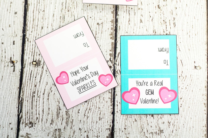 Pink and aqua Ring Pop Valentines on white wood background after being printed and cut out