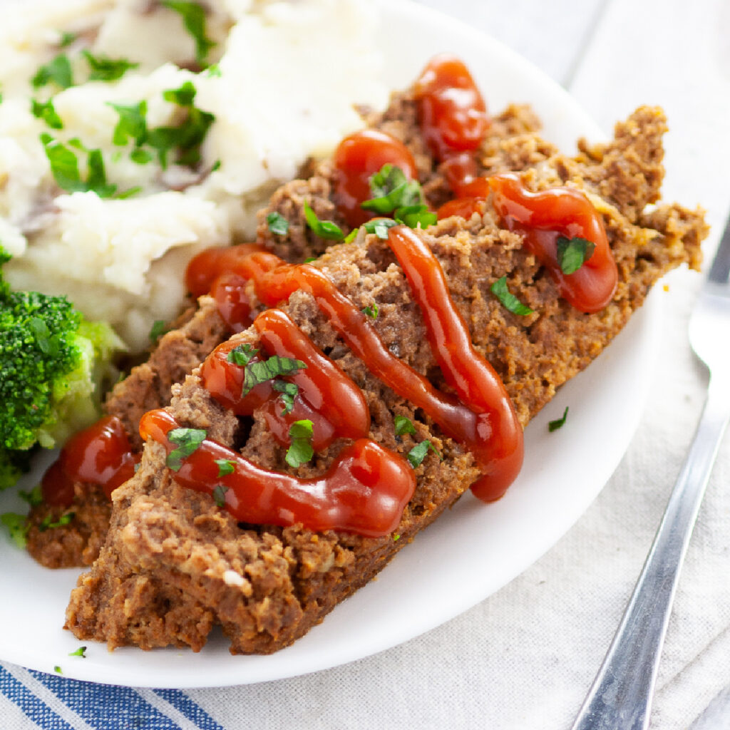Close up of two slices of slow cooker meatloaf on a small plate drizzled with ketchup