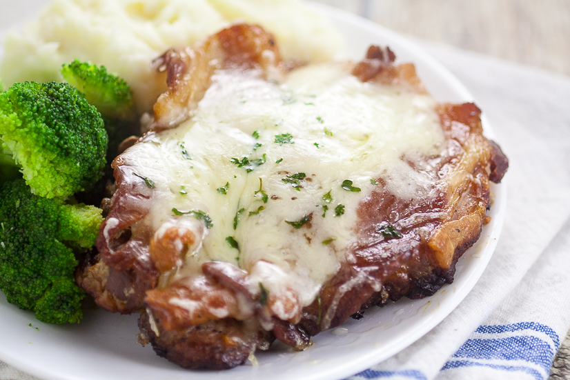 Thick cut pork chops with bacon and swiss cheese on white plate with veggies and potatoes.