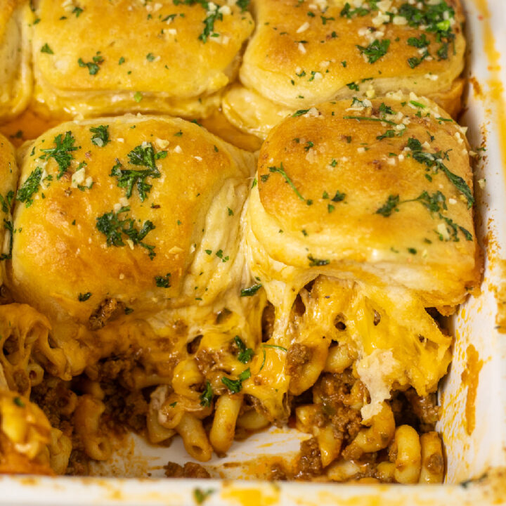 Cheeseburger casserole topped with buttery biscuits and fresh parsley in a casserole dish with a scoop missing.