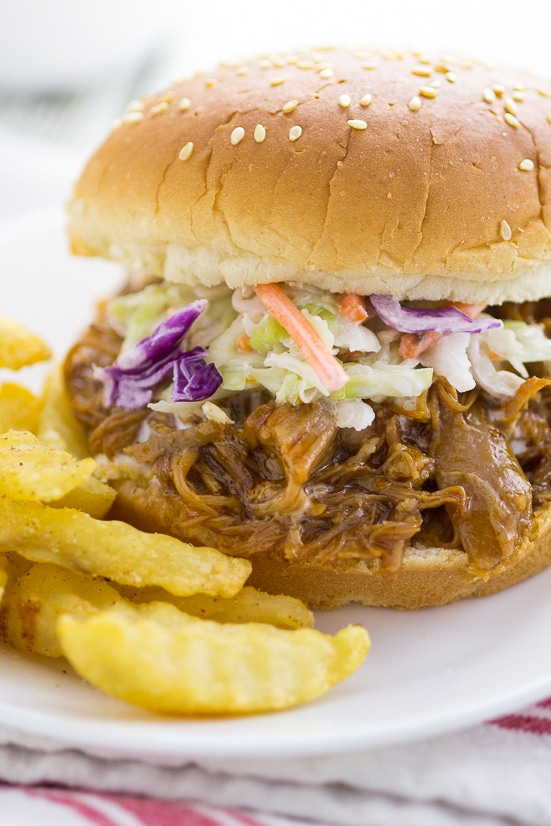 Close up photo of a pulled pork sandwich topped with coleslaw next to crinkle cut French fries