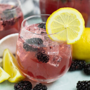 Blackberry lemon spritzer in a stemless wine glass with ice and fresh blackberries with a lemon slice on the rim.