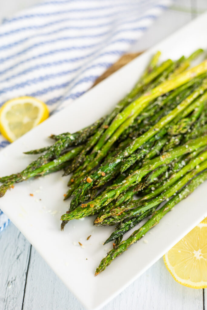 Oven roasted asparagus on a white rectangular plate next to lemon slices and