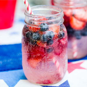 Berry spritzer with frozen strawberries and blueberries and a red striped straw in a mason jar.