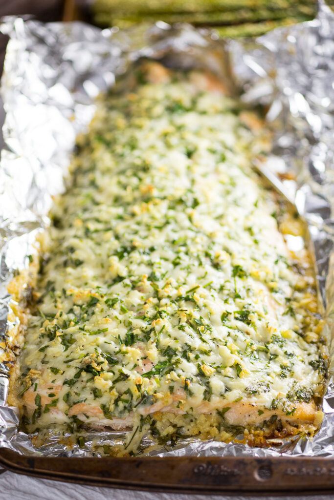 Close up of parmesan garlic herb salmon on foil on a baking sheet.