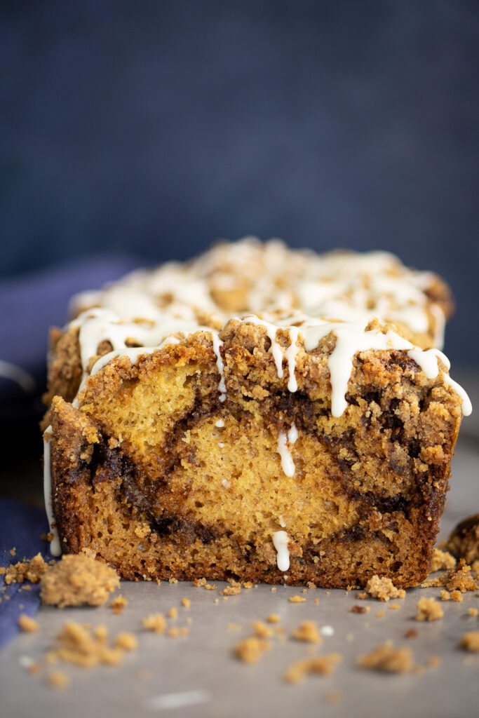 A slice of cinnamon swirl loaf cake showing the interior cinnamon swirls with vanilla glaze dripping down in front of a navy blue background.