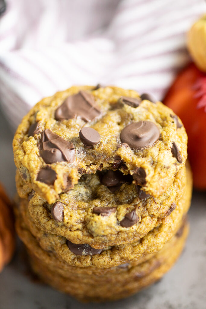 Overhead view of a stack of pumpkin chocolate chip cookies with a bite taken out of the top one and a linen napkin behind.
