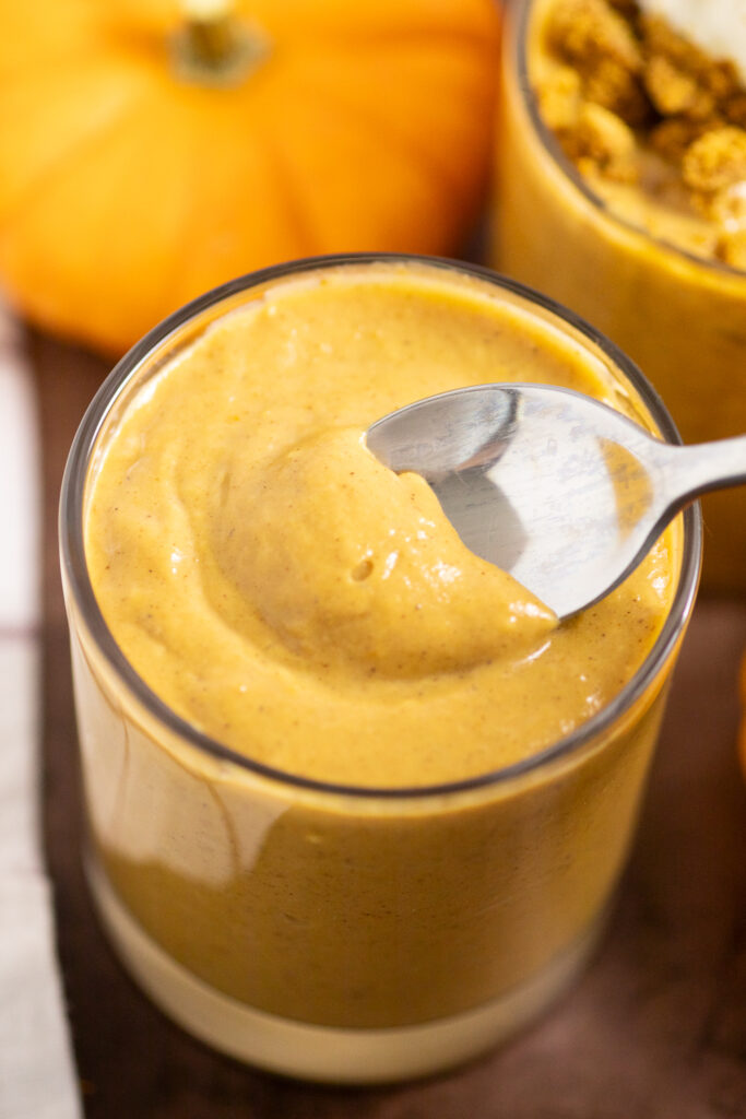 A spoon taking a bite out of a cup of creamy pumpkin pudding.