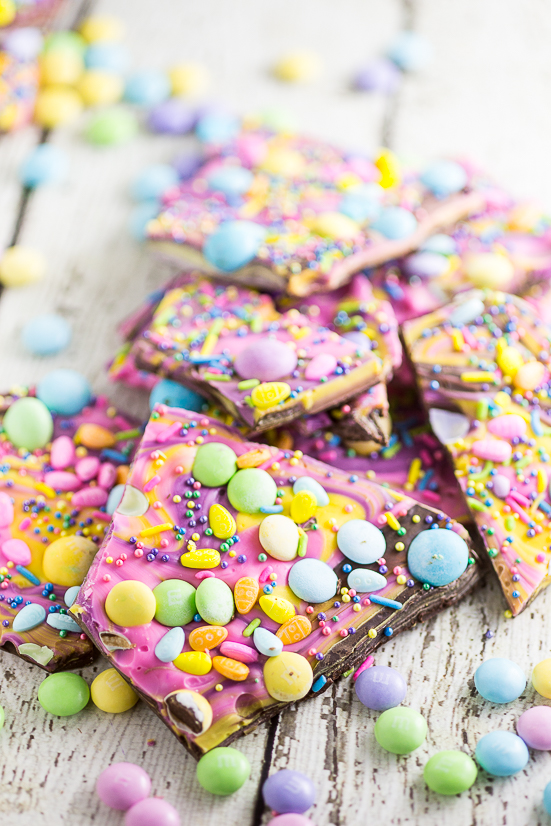 Pile of colorful swirled chocolate Easter bark with pastel Easter candies on a white wood background