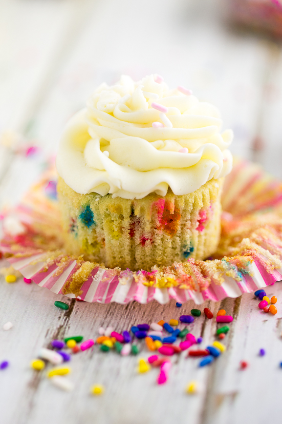 Unwrapped funfetti cupcake topped with buttercream surrounded by rainbow sprinkles