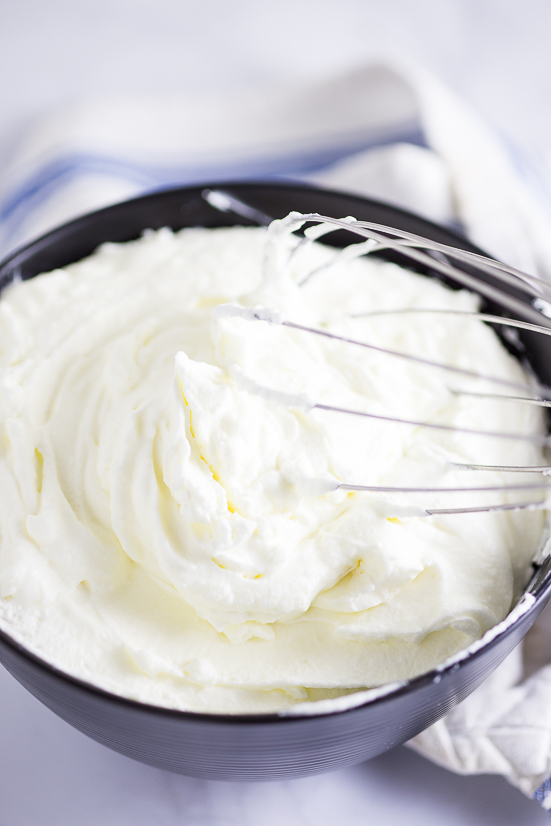 Black bowl filled with homemade whipped cream with a whisk in the bowl.