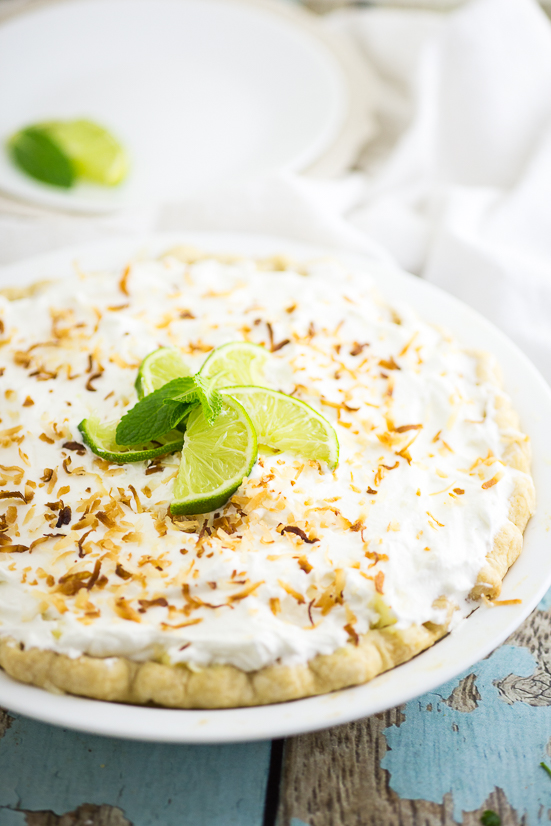Full coconut cream pie topped with toasted coconut and lime wedges on a rustic wood background