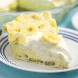 A slice of banana cream pie on a small white plate with blue stripes around the rim.