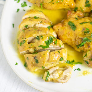 Maple mustard chicken on a plate with maple mustard sauce topped with freshly chopped parsley. The chicken is cut into slices.