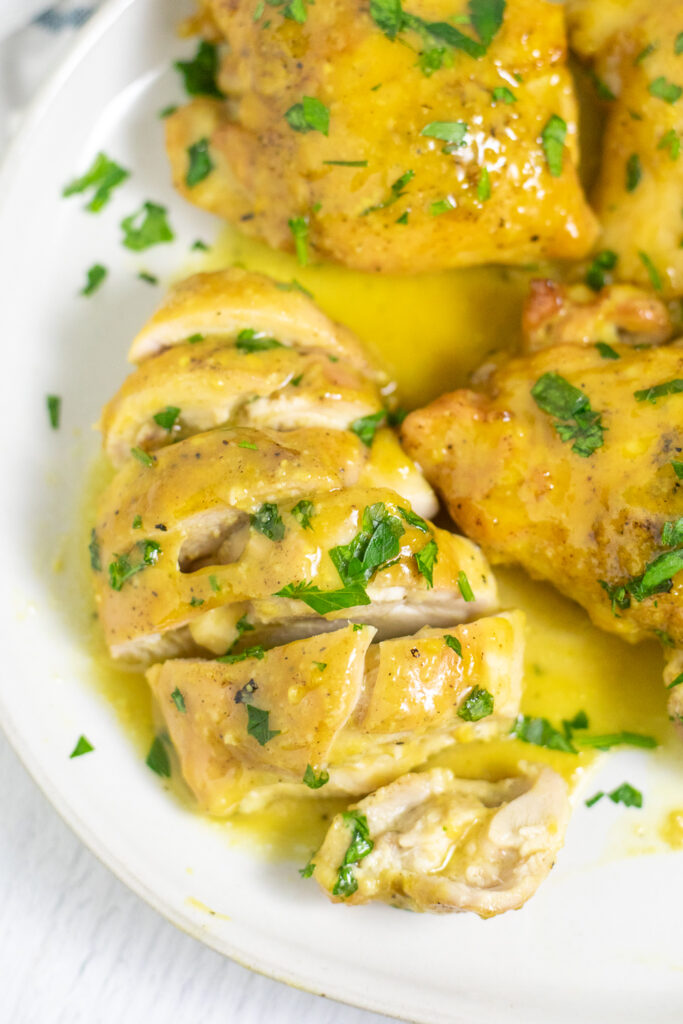 Maple mustard chicken on a plate with maple mustard sauce topped with freshly chopped parsley. The chicken is cut into slices.