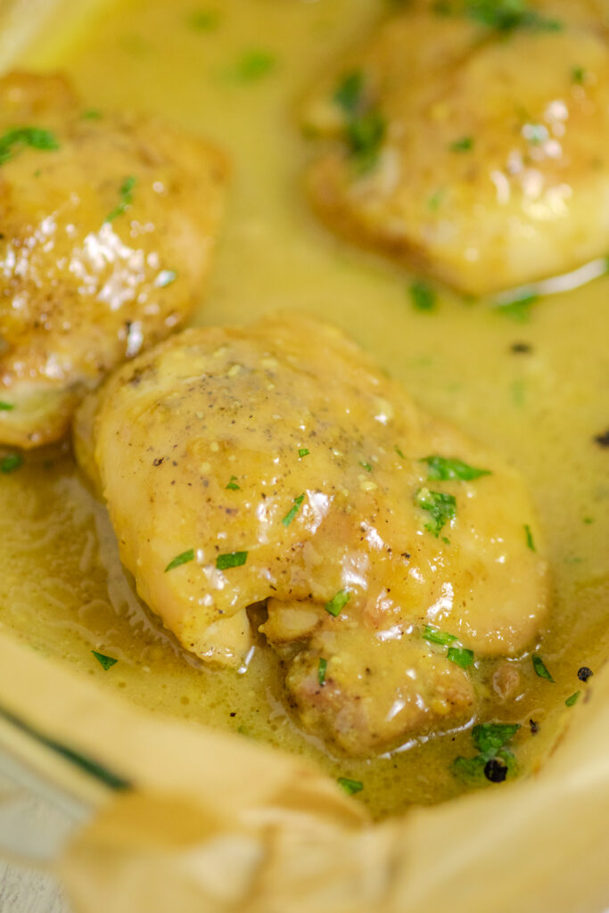 Maple mustard chicken in a baking dish lined with brown parchment paper and topped with fresh parsley.