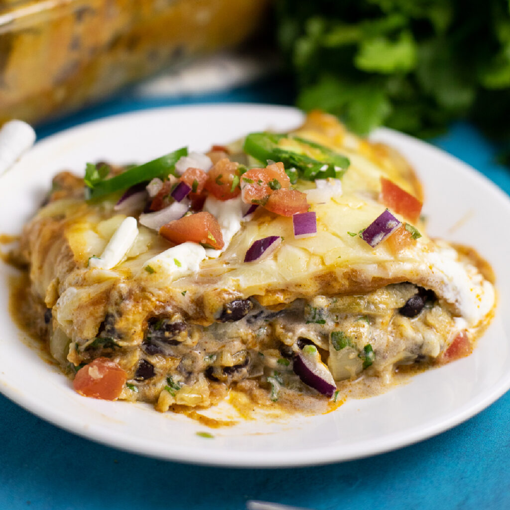Sideview of a piece of black bean enchilada casserole on a small white plate