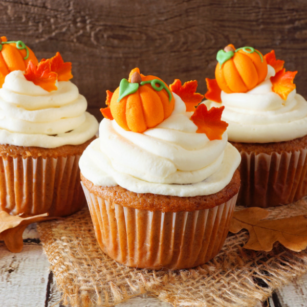3 frosted cupcakes sitting on burlap, topped with fondant pumpkins and leaves