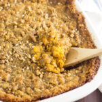 Wooden Spoon in the middle of a southern sweet potato casserole topped with brown sugar pecan streusel.