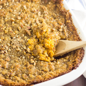 Wooden Spoon in the middle of a southern sweet potato casserole topped with brown sugar pecan streusel.